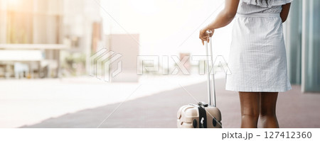 Cropped of woman walking away from the camera with a piece of luggage. She is wearing a light-colored dress and appears to be in an urban setting, copy space Cropped of woman walking away from the camera with a piece of luggage. She is wearing a light-colored dress and appears to be in an urban setting, copy space 127412360