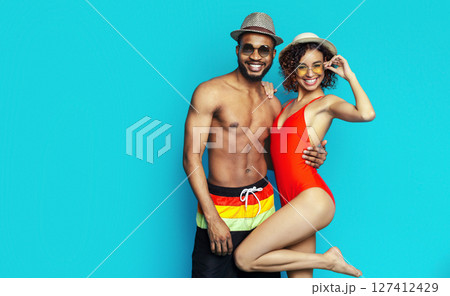 African American young couple wearing swimwear and hats, posing against a bright blue background. They both appear happy and relaxed, enjoying the summer weather. African American young couple wearing swimwear and hats, posing against a bright blue background. They both appear happy and relaxed, enjoying the summer weather. 127412429
