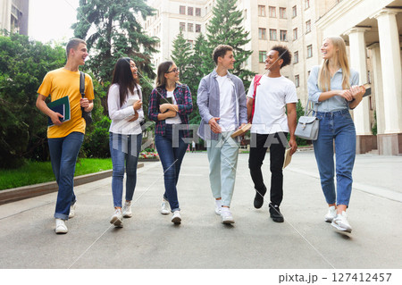 Happy students walking outside the university building, having break after classes Happy students walking outside the university building, having break after classes 127412457