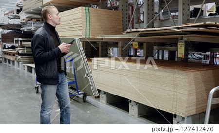 Man shopping for wood panels in hardware store using smartphone app for diy project. Technology aids decision making in construction industry. translator: good price Man shopping for wood panels in hardware store using smartphone app for diy project. Technology aids decision making in construction industry. translator: good price 127412470