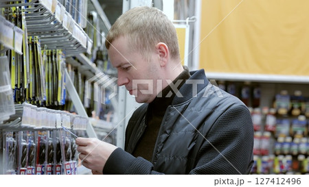 Man carefully selects drill bits from shelf while shopping in hardware store. A man in a hardware store choosing a tool. 127412496