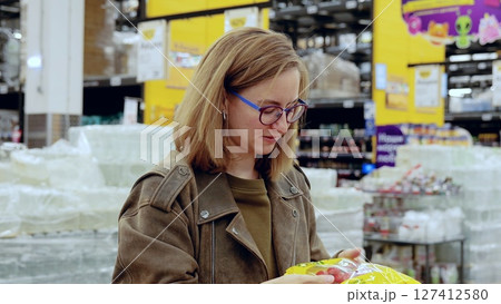 Young woman carefully selecting fresh tomatoes from a bag in the produce section of a modern supermarket, focusing on quality and ripeness Young woman carefully selecting fresh tomatoes from a bag in the produce section of a modern supermarket, focusing on quality and ripeness 127412580