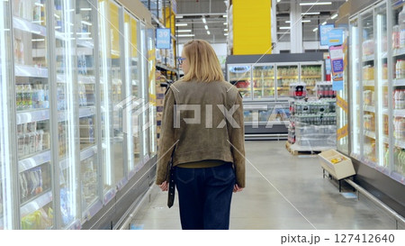Young woman strolling through the grocery store, carefully selecting items from the chilled display case 127412640