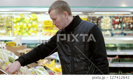 Man choosing fresh vegetables at grocery store, highlighting healthy eating, vegetarian diets, and budget friendly meal planning. Man choosing fruits in supermarket, shelf with apples 127412642