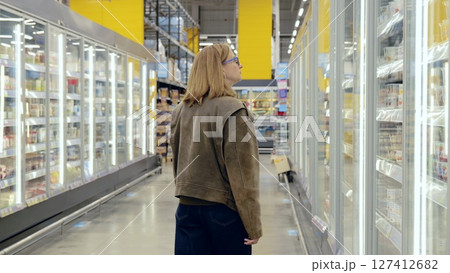 Young woman browsing refrigerated dairy products in a grocery store, walking through the aisles of chilled shelves 127412682