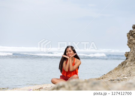 Happy woman sitting on the beach with waves in the background 127412700