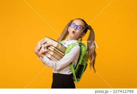 Going To School. Surprised Nerdy Schoolgirl Carrying Heavy Books On Yellow Background In Studio. Empty Space For Text 127412799