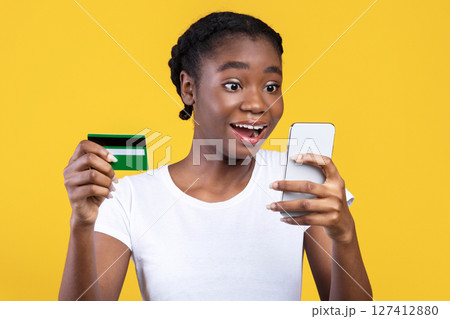 Mobile Shopping. Excited Black Woman Holds Credit Card And Smartphone, Shops Online Via Application Standing Over Yellow Studio Background. Excited Customer, Shopping App And Cashback Mobile Shopping. Excited Black Woman Holds Credit Card And Smartphone, Shops Online Via Application Standing Over Yellow Studio Background. Excited Customer, Shopping App And Cashback 127412880