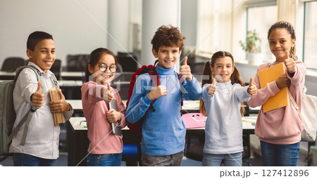 Education Concept. Diverse group of happy smiling international classmates standing in line with notebooks and backpacks in classroom and showing thumbs up sign gesture, enjoying studying at school Education Concept. Diverse group of happy smiling international classmates standing in line with notebooks and backpacks in classroom and showing thumbs up sign gesture, enjoying studying at school 127412896