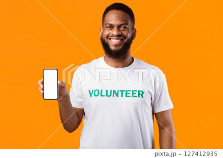 African American Volunteer Man Shows Blank Smartphone Screen Smiling To Camera Standing Over Yellow Studio Background. Great Mobile Application For Volunteering Concept. Mockup African American Volunteer Man Shows Blank Smartphone Screen Smiling To Camera Standing Over Yellow Studio Background. Great Mobile Application For Volunteering Concept. Mockup 127412935