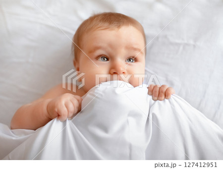 Closeup of adorable blonde baby laying in bed under blanket. Happy little kid infant woke up after sleeping, playing with duvet and looking at copy space, lying in baby bed Closeup of adorable blonde baby laying in bed under blanket. Happy little kid infant woke up after sleeping, playing with duvet and looking at copy space, lying in baby bed 127412951