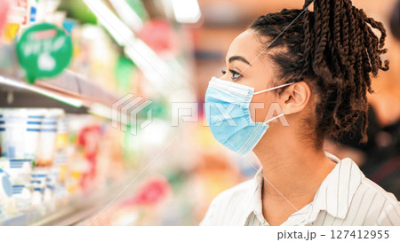 African Lady Wearing Face Mask Shopping Food Products And Groceries In Supermarket, Standing Near Shelves In Shop Aisle Choosing Goods In Groceries Store Indoors. Female Customer Buyer Portrait African Lady Wearing Face Mask Shopping Food Products And Groceries In Supermarket, Standing Near Shelves In Shop Aisle Choosing Goods In Groceries Store Indoors. Female Customer Buyer Portrait 127412955