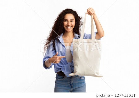 Use Eco Bag. Smiling Woman Pointing Finger At White Textile Shopper Handbag Standing Over White Studio Background. Eco-Friendly Lifestyle, Fashion And Ecology, Stop Using Plastic Concept Use Eco Bag. Smiling Woman Pointing Finger At White Textile Shopper Handbag Standing Over White Studio Background. Eco-Friendly Lifestyle, Fashion And Ecology, Stop Using Plastic Concept 127413011