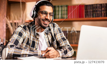 Positive Indian Student Guy At Laptop Computer Learning Online Having Remote Class With Distant Teacher Sitting At Home, Wearing Headphones. Modern Education, E-Learning And E-Teaching Concept Positive Indian Student Guy At Laptop Computer Learning Online Having Remote Class With Distant Teacher Sitting At Home, Wearing Headphones. Modern Education, E-Learning And E-Teaching Concept 127413070