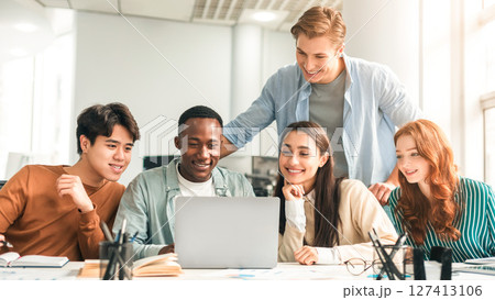 Studying Together. Group of diverse multiracial students sitting at desk in auditorium using laptop, watching tutorial or educational video, doing research and making project for college Studying Together. Group of diverse multiracial students sitting at desk in auditorium using laptop, watching tutorial or educational video, doing research and making project for college 127413106