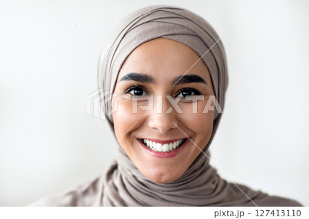 Portrait of cheerful young woman in hijab doctor or patient over clinic interior, copy space. Muslim lady in beautiful headscarf physician smiling at camera, working at clinic, closeup 127413110