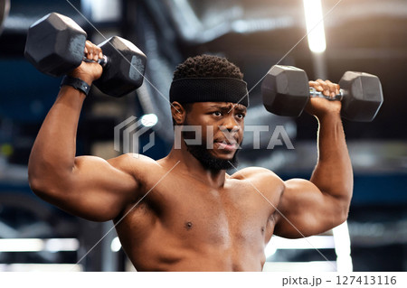 Confident african american shirtless man bodybuilder with muscular body exercising at gym, lifting up dumbbells, making work out for his biceps and back, looking at copy space Confident african american shirtless man bodybuilder with muscular body exercising at gym, lifting up dumbbells, making work out for his biceps and back, looking at copy space 127413116
