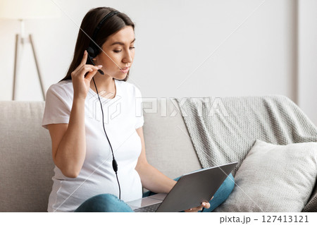 Young Pregnant Woman With Headset And Laptop At Home Study Or Working Remotely, Millennial Expectant Woman Sitting At Couch With Computer, Learning Online Or Having Distance Job, Free Space 127413121