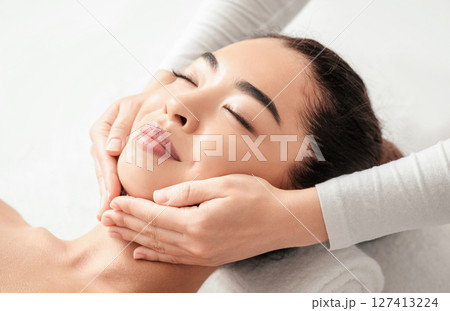 Face Massage. Closeup of attractive asian woman getting beauty treatment at spa salon, relaxed young korean lady enjoying skin and body care, lying on massage table with closed eyes, free space Face Massage. Closeup of attractive asian woman getting beauty treatment at spa salon, relaxed young korean lady enjoying skin and body care, lying on massage table with closed eyes, free space 127413224