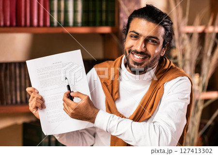 Happy Indian Teacher Man Showing Essay To Camera Having Online Webinar Lecture With Distant Students Sitting Indoors. Remote Tutoring, Distance Education And Learning Concept 127413302