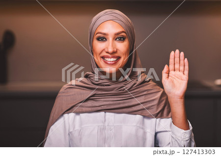 Online Video Call. Muslim Lady In Hijab Waving Hand To Camera Sitting In Kitchen At Home. Happy Arab Woman Communicating Via Video Conference, Remote Communication Concept Online Video Call. Muslim Lady In Hijab Waving Hand To Camera Sitting In Kitchen At Home. Happy Arab Woman Communicating Via Video Conference, Remote Communication Concept 127413303