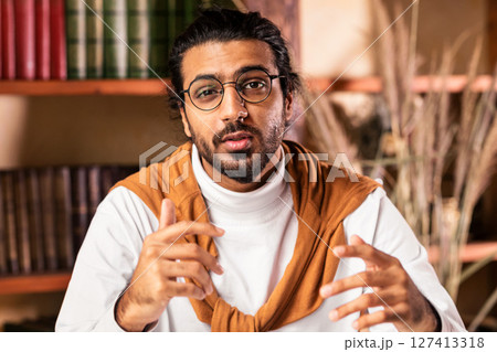 Distant Indian Teacher Guy Talking To Camera Having Online Lecture Or Webinar Teaching Remotely Sitting Indoors, Working From Home. Tutoring And E-Teaching, Remote Education Concept 127413318
