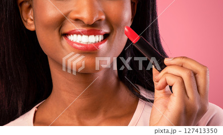 Lovely black woman holding bright lipstick on pink studio background. Charming African American lady putting on makeup, advertising cosmetic product. Beauty and fashion concept 127413350