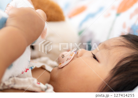 One year old asian girl comforts herself with toy in cozy bedroom environment One year old asian girl comforts herself with toy in cozy bedroom environment 127414255