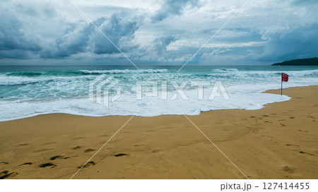 Waves crashing sandy beach with warning flag coastal area nature landscape dramatic clouds 127414455