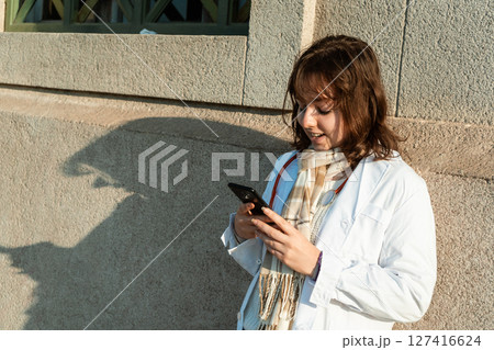 Young doctor checking phone during a break outside the medical center 127416624