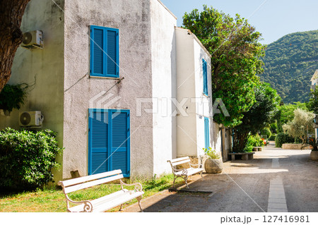 White building with blue shutters and arches surrounded by garden. Mediterranean architecture, serene vacation atmosphere, and hotel patio concept. 127416981