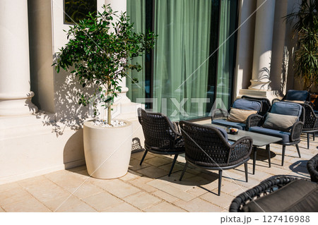 Modern terrace with potted tree and cushioned seating outside hotel. Urban comfort, hospitality design, and stylish outdoor relaxation concept. 127416988
