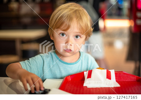 Young child enjoying fast food meal in a casual dining environment. Four year old boy happily eating in a restaurant. Kids diet, bad food choices, early junk food addiction Young child enjoying fast food meal in a casual dining environment. Four year old boy happily eating in a restaurant. Kids diet, bad food choices, early junk food addiction 127417165