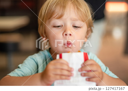 Young child enjoying fast food meal in a casual dining environment. Four year old boy happily eating in a restaurant. Kids diet, bad food choices, early junk food addiction 127417167