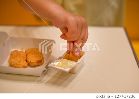 A small child wearing a yellow shirt is eating chicken nuggets in a vibrant environment. Four year old boy enjoying fast food meal. Kids diet, bad food choices, early junk food addiction A small child wearing a yellow shirt is eating chicken nuggets in a vibrant environment. Four year old boy enjoying fast food meal. Kids diet, bad food choices, early junk food addiction 127417236