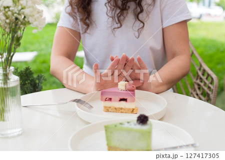 Woman Gesturing Near Colorful Cakes on White Plates in Outdoor Setting. No to sugar, diet concept, fasting, dieting, losing weight. No cakes, woman on a diet. 127417305