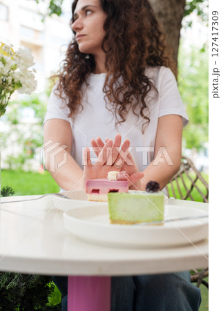 Woman Gesturing Near Colorful Cakes on White Plates in Outdoor Setting. No to sugar, diet concept, fasting, dieting, losing weight. No cakes, woman on a diet. 127417309