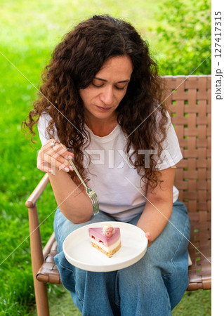 A woman seated at an outdoor table with two plates of desserts, enjoying the scenery and calm surroundings in a peaceful green garden. diet concept, fasting, dieting, losing weight, woman on a diet. A woman seated at an outdoor table with two plates of desserts, enjoying the scenery and calm surroundings in a peaceful green garden. diet concept, fasting, dieting, losing weight, woman on a diet. 127417315