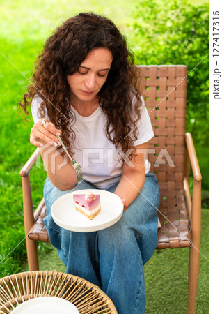 A woman seated at an outdoor table with two plates of desserts, enjoying the scenery and calm surroundings in a peaceful green garden. diet concept, fasting, dieting, losing weight, woman on a diet. A woman seated at an outdoor table with two plates of desserts, enjoying the scenery and calm surroundings in a peaceful green garden. diet concept, fasting, dieting, losing weight, woman on a diet. 127417316