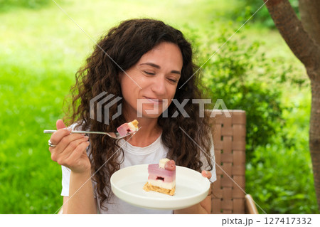 A young woman sits outdoors enjoying a delicious dessert, surrounded by nature and peaceful greenery. The setting reflects relaxation, savoring sweet moments, and a connection with nature. A young woman sits outdoors enjoying a delicious dessert, surrounded by nature and peaceful greenery. The setting reflects relaxation, savoring sweet moments, and a connection with nature. 127417332