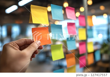 Manager placing sticky notes on glass wall in office for brainstorming session Manager placing sticky notes on glass wall in office for brainstorming session 127417557