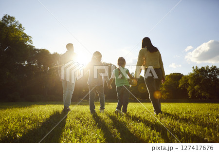 Family walking together in grassy green field, close holding hands towards sun 127417676