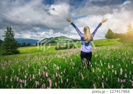 Young woman raising arms standing in a field of pink flowers 127417968