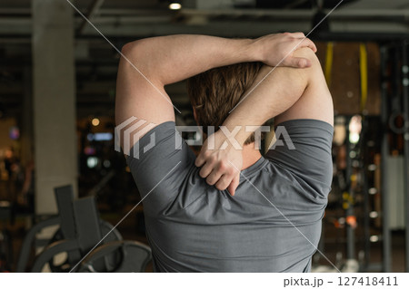 Athlete or caucasian young sporty man doing stretching back and arms at gym before workout. Training, wellness and athlete man workout. Preparation for exercise at health club. Back View 127418411