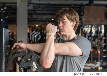 Athlete or caucasian young sporty man doing stretching back and arms at gym before workout. Training, wellness and athlete man workout. Preparation for exercise at health club. 127418412