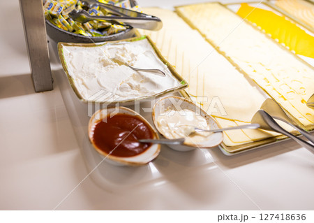 Cheese slices and sauces served on a buffet table for breakfast. Hotel catering, dairy selection, and condiment variety concept. 127418636