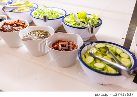 Fresh vegetables and toppings served in white bowls on buffet table. Healthy eating, salad bar variety, and hotel breakfast concept. 127418637