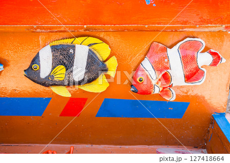 Colorful fish decorations on painted surface. Marine theme, children attraction, and playful coastal design. 127418664