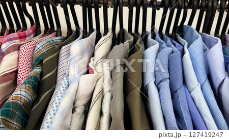 Many colorful men's shirts hang on hangers in the store. Men's wardrobe. 127419247