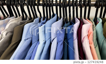 A woman's hand sorts through men's shirts that hang on hangers in a store. 127419248